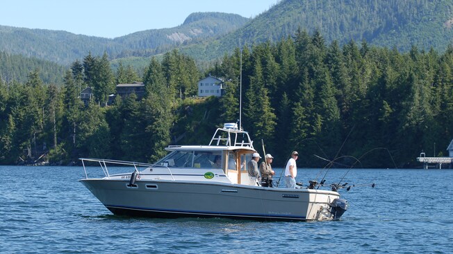 Three men fish off the back of a motor boat