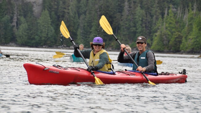 A man and a woman wearing life jackets paddle together in a kayak