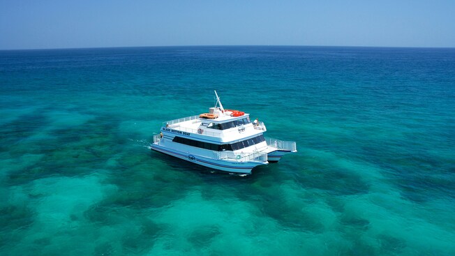 A double decker catamaran sits on the open water over a large reef