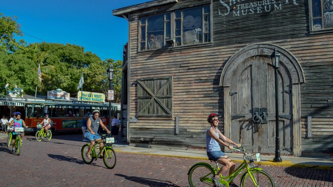 A group of cyclists riding next to a clapboard building with a sign that reads Shipwreck Treasure Museum