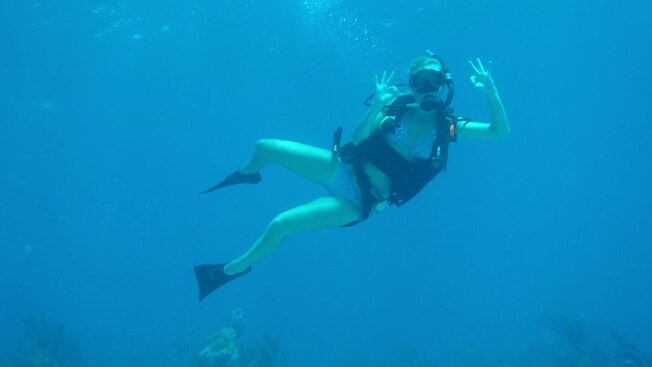 A female scuba diver forms the OK signal with her hands underwater