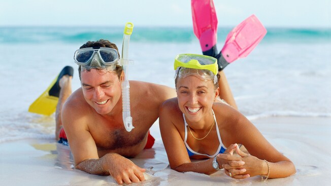 Un hombre y una mujer recostados en la playa con máscaras de esnórquel en la cabeza y aletas en los pies