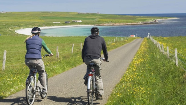 Two bicycle riders riding throught he countryside toward a coastal inlet