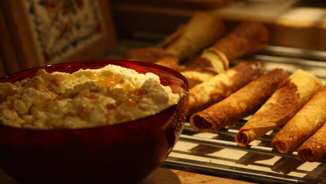 Uma tigela com recheio de creme e uma prateleira de biscoitos cheia de biscoitos de waffle finos enrolados em cones