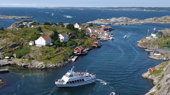 A boat filled with passengers sails through a series of rocky islets dotted with mariners homes A boat filled with passengers sails through a series of rocky islets dotted with mariners homes