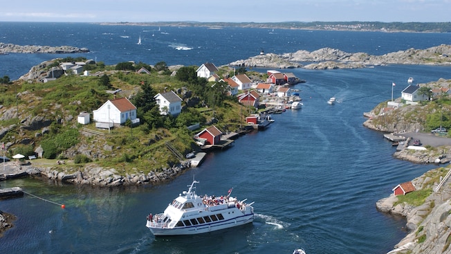 Un bote lleno de pasajeros que navega por una serie de islotes rocosos con casas de marineros Un bote lleno de pasajeros que navega por una serie de islotes rocosos con casas de marineros