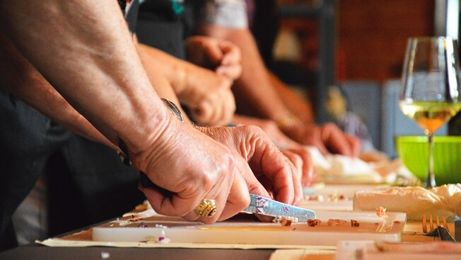 A pair of hands using a knife to chop ingredients on a cutting board