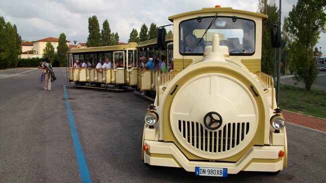 A tour guide speaks into a microphone to a group of tourists on a trolley train