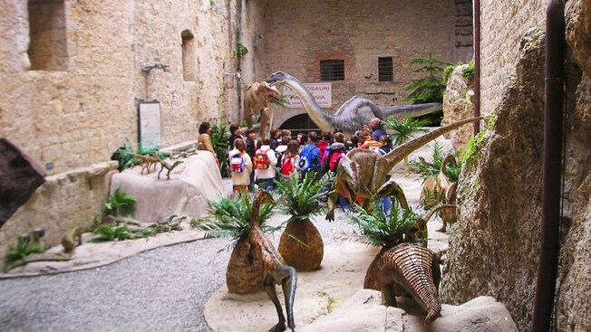 A group of children learn about dinosaurs as they view a dinosaur display in an open area of a stone castle