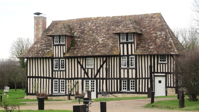 A half timbered building featuring windows, a chimney and a lawn with trees