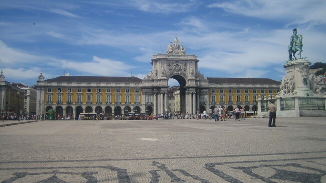 Estatua de un hombre a caballo frente a un gran edificio antiguo con un arco decorado en el centro