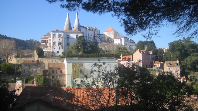 Um grande edifício com duas estruturas cônicas em seu telhado fica em uma encosta com vista para um centro histórico Um grande edifício com duas estruturas cônicas em seu telhado fica em uma encosta com vista para um centro histórico