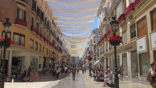 A city street shaded by sheets and lined with storefronts, street lights and people