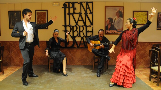 2 dancers stand by a seated dancer and a man with a guitar