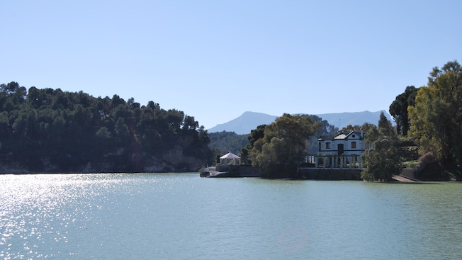A house near a gazebo, trees, mountains and a lake