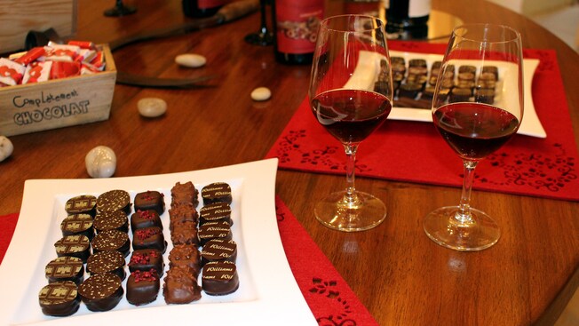 A table set with a plate of chocolates and 2 stemmed glasses filled with wine