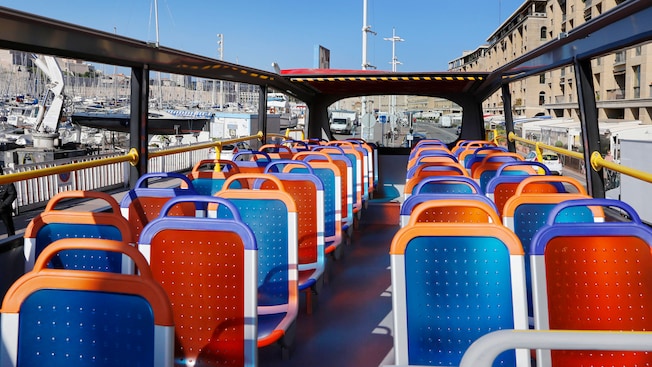 Um ônibus turístico com capota aberta estacionado próximo a um pequeno porto à beira-mar cheio de barcos a vela Um ônibus turístico com capota aberta estacionado próximo a um pequeno porto à beira-mar cheio de barcos a vela