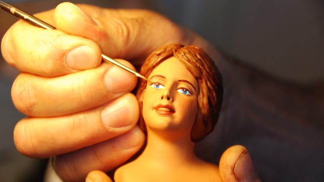 Uma mão pintando o rosto de uma estatueta feminina Uma mão pintando o rosto de uma estatueta feminina