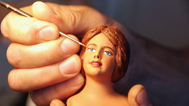 A hand painting a female figurine's face
