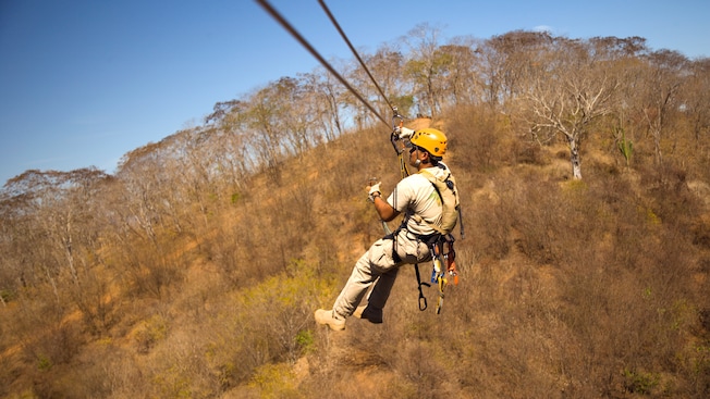 Un hombre con un casco que se lanza en tirolesa sobre unos árboles