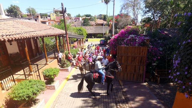 A crowd of people watch a man seated atop a horse against the backdrop of small houses