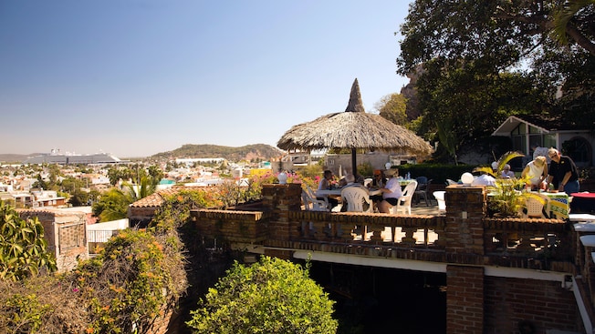 Personas sentadas en una mesa bajo una palapa en una terraza al aire libre