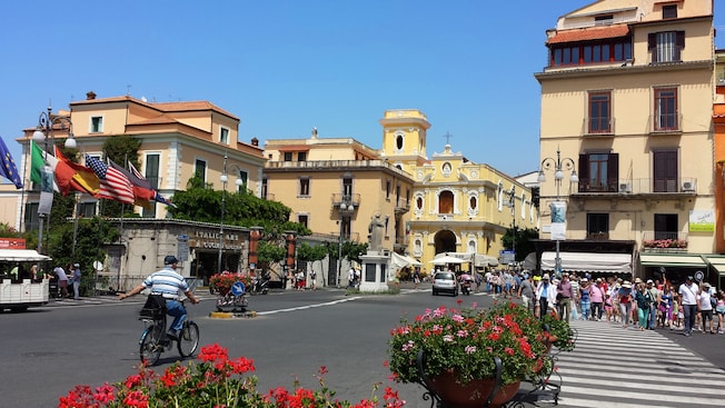 Pedestrians exploring the town of Sorrento on a street lined with flowers, trees and charming architecture. Pedestrians exploring the town of Sorrento on a street lined with flowers, trees and charming architecture.