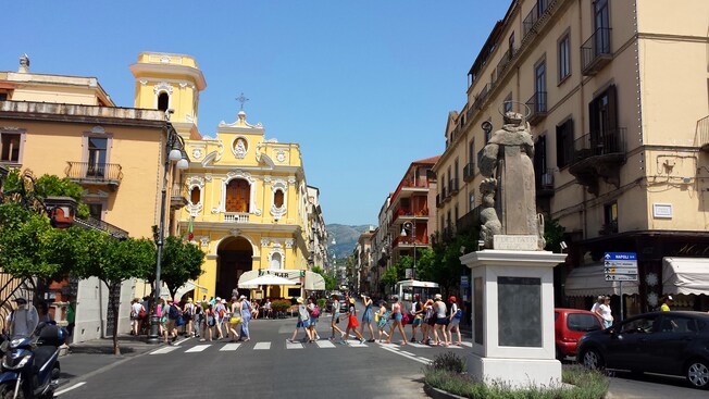 Un grupo de visitantes cruza una concurrida, pero encantadora calle bordeada de árboles