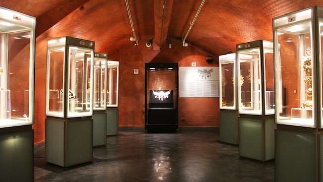 Reliquias brillantes en vitrinas de vidrio se alinean en los muros de un espacio de exhibición con un techo arqueado