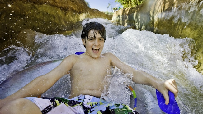 A boy smiles widely as he holds the handle of an inner tube on a water ride A boy smiles widely as he holds the handle of an inner tube on a water ride