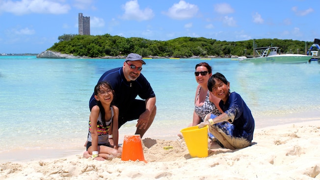 A smiling couple and their 2 young kids build sandcastles on the beach using pails and shovels A smiling couple and their 2 young kids build sandcastles on the beach using pails and shovels