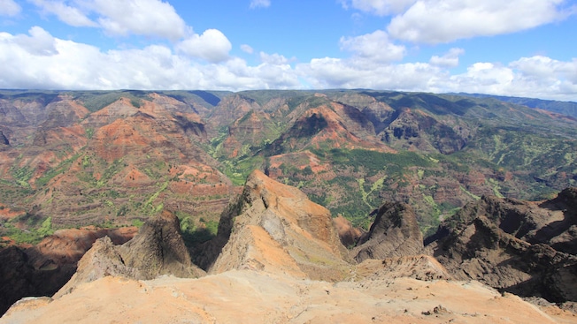 A large, rocky canyon with patches of grass and foliage and the shadows of clouds