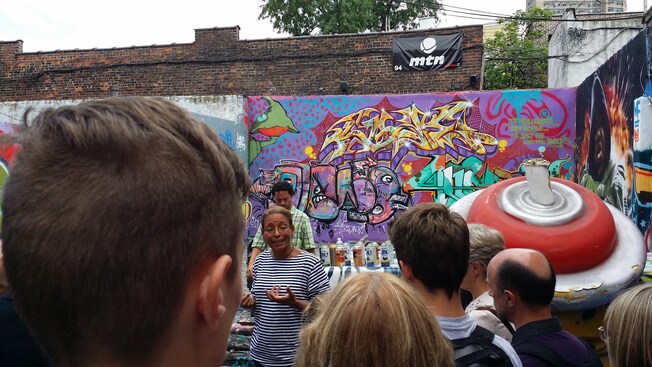 Una mujer habla con una multitud frente a una pared con grafiti artístico