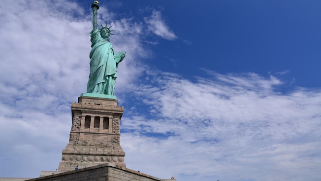 Una estatua de una mujer con una túnica que sostiene un libro con la mano izquierda y levanta una antorcha por encima de la cabeza con la otra Una estatua de una mujer con una túnica que sostiene un libro con la mano izquierda y levanta una antorcha por encima de la cabeza con la otra