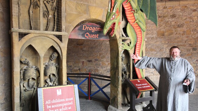 A man in period garb gestures to an entry sign that says Dragon Quest
