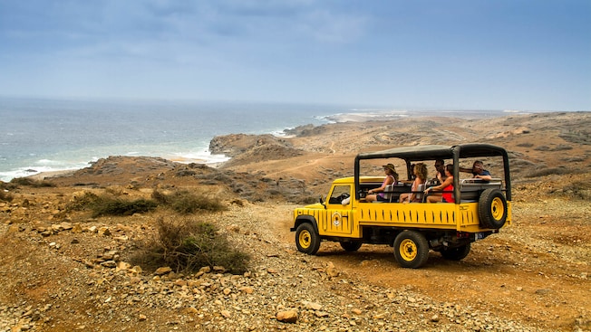 An open air Land Rover Defender filled with passengers is stopped on an undeveloped rocky terrain looking out to the ocean An open air Land Rover Defender filled with passengers is stopped on an undeveloped rocky terrain looking out to the ocean