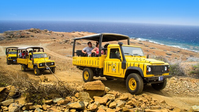 Land Rover Defenders carrying passengers across rocky terrain overlooking the ocean Land Rover Defenders carrying passengers across rocky terrain overlooking the ocean
