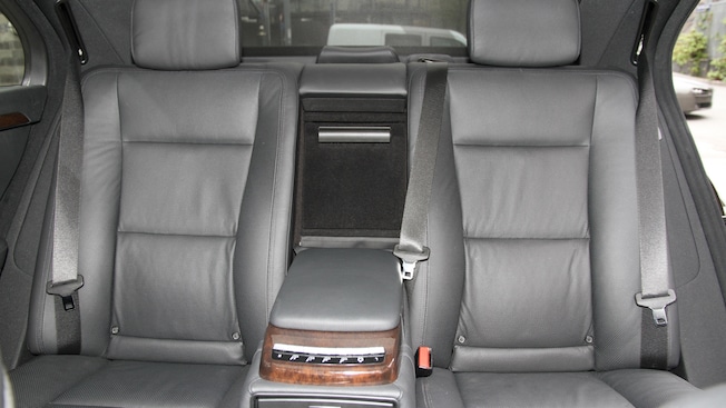 The rear, leather seats of a car with a console between them and a car door open The rear, leather seats of a car with a console between them and a car door open