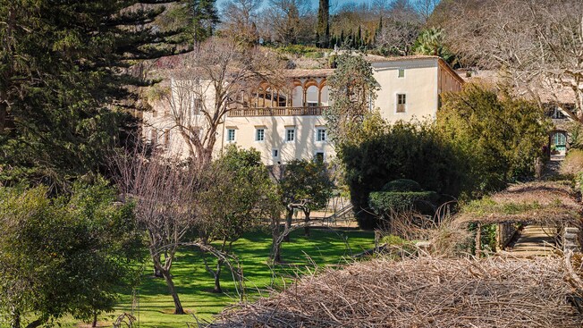 A multi level country manor is surrounded by trees and contains an arched column terrace on the top level