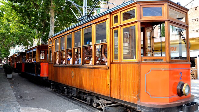 Passengers waiting at a train stop in a vintage trolley car train with open windows
