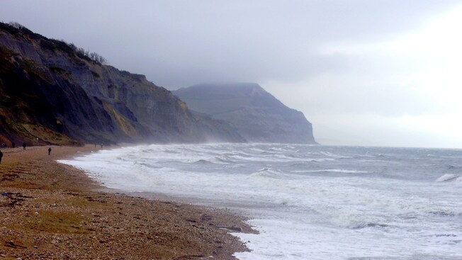 People walking along a sandy coastline between cliffs and ocean