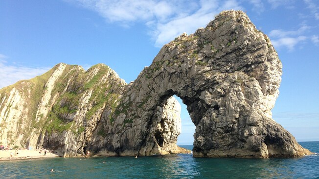 A crowded beach on the Jurassic Coast is situated next to the Durdle Door natural limestone arch
