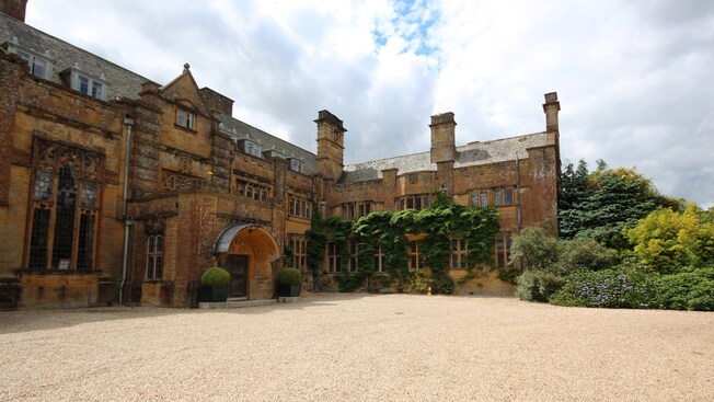The gravel entrance to a 17th century stone manor surrounded by gardens