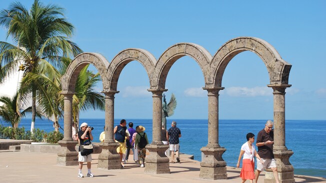 Una estructura con cuatro arcos en el mirador de un acantilado, con turistas que admiran el océano