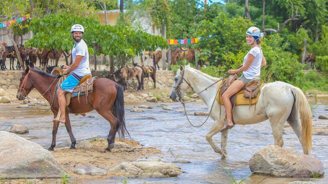 A man and a woman horseback ride through a shallow stream