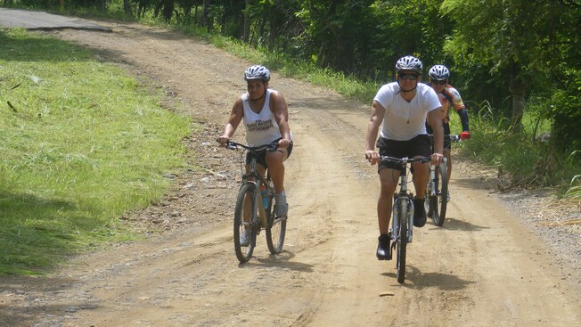 3 people ride bikes down a road