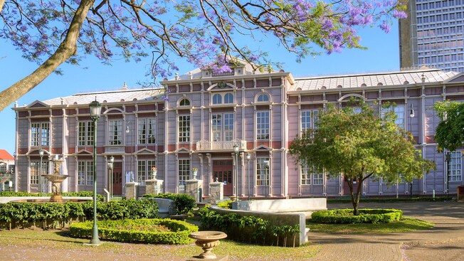 A large building surrounded by a garden, a fountain and trees