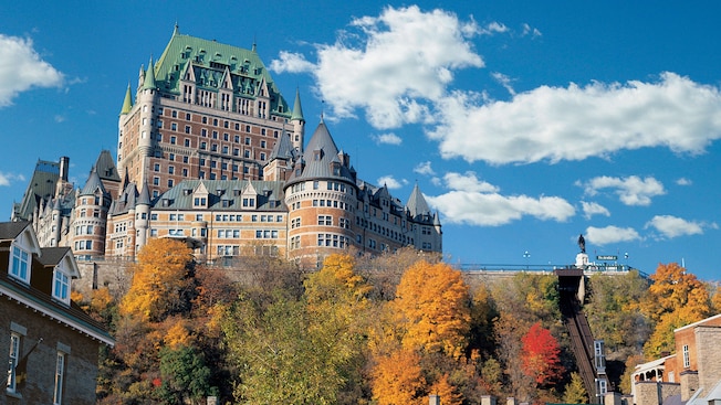 A grand chateau towers over trees and quaint buildings below A grand chateau towers over trees and quaint buildings below