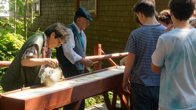 Guests observe a man and a woman making maple taffy pops during a demonstration