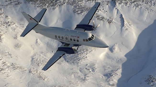 A turboprop aircraft flies over a snow covered mountain landscape